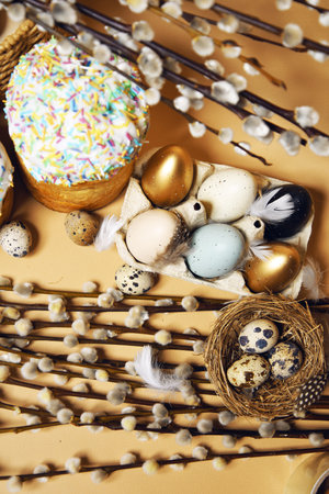 Easter holidays, pussy willow, colorful painted eggs in a tray, quail eggs in a nest, a basket with Easter cake on a nude background, warm. Religion and traditionsの写真素材