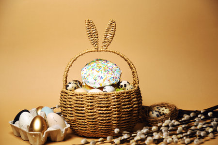 Easter holidays, pussy willow, colorful painted eggs in a tray, quail eggs in a nest, a basket with Easter cake on a nude background, warm. Religion and traditionsの写真素材