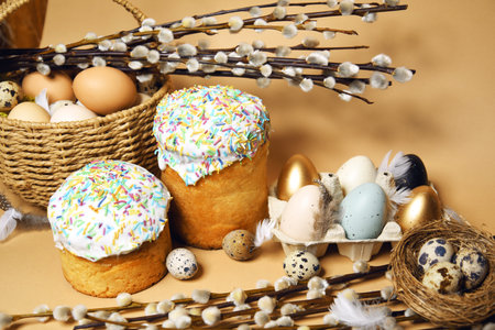 Easter holidays, pussy willow, colorful painted eggs in a tray, quail eggs in a nest, a basket with Easter cake on a nude background, warm. Religion and traditionsの写真素材