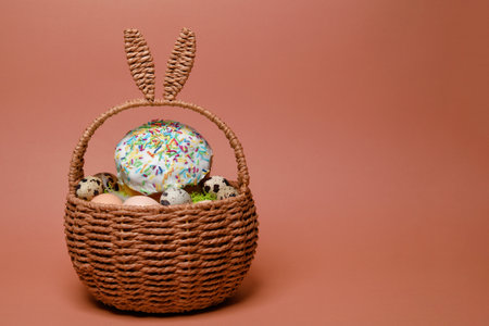 Easter decorations in a basket with rabbit ears. Easter cake and eggs on moss, quail eggs and feathers on a pink background. Place for textの写真素材