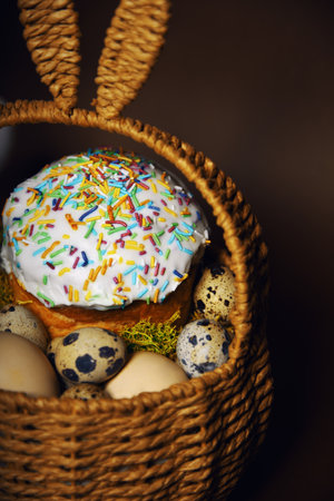 Easter holidays, cute basket with bunny ears on brown background. Easter cakes with colored sprinkles, colored golden eggs, and pussy willow decorations. Nest with eggs, Traditionsの写真素材