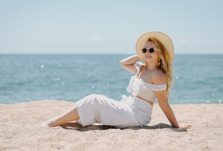 Portrait of a beautiful young woman in a hat and sunglasses sitting on the beachの写真素材