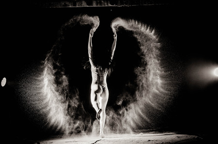 The girl with the flour on the body stretches the arms up with thrown flour on black background black and white image.の写真素材