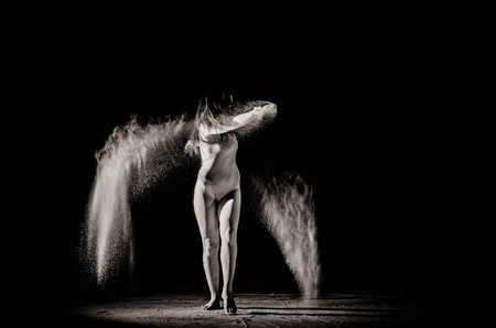 The girl with the flour on the body stretches the arms up with thrown flour on black background black and white image.の写真素材