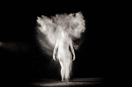 The girl with the flour on the body stretches the arms up with thrown flour on black background black and white image.の写真素材