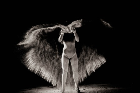 The girl with the flour on the body stretches the arms up with thrown flour on black background black and white image.の写真素材