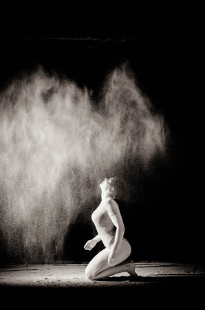 The girl with the flour on the body stretches the arms up with thrown flour on black background black and white image.の写真素材