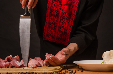 Female hands with a knife in their hand cut fresh meat on a tableの写真素材