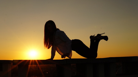 Young girl in sports uniform sits on the edge of the roof during sunsetの写真素材
