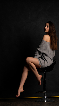beautiful sexy girl, posing a short gray dress, black background chairの写真素材