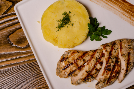 closeup two pieces of medium raw grilled meat decorated with red pepper and sauce served with potato chips and vegetable salad on black restaurant plate on wooden tableの写真素材