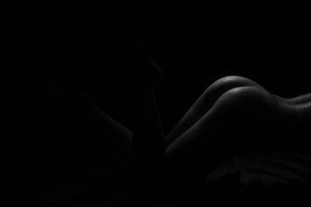 Black and White Beautiful woman body. Fashion art studio portrait of elegant naked lady with shadow on her. Female stomach isolated on black background. Erotic pose low key shootの写真素材
