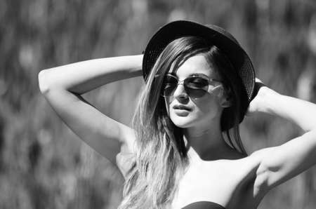 Girl in a hat and glasses in a swimsuit posing on the beachの写真素材