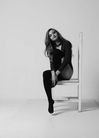 Young happy fitness girl with sporty body posing at studio on a blue background. Beautiful fit Girl. Fitness model in white sports bodysuit sitting on chair. Healthy lifestyle. Sexy womanの写真素材