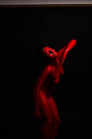 creative portrait of a young girl. The face is painted with red glitter paint. The triangle is drawn on the face. Model in profile on black backgroundの写真素材