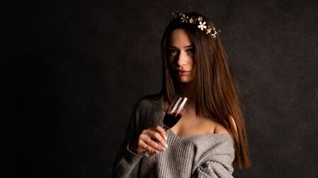 Sexy young blonde in beautiful Gray tight shiny dress with sleeves and in high suede boots posing in the studio on the chair. On a black background using red light filtersの写真素材