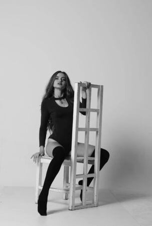 Young happy fitness girl with sporty body posing at studio on a blue background. Beautiful fit Girl. Fitness model in white sports bodysuit sitting on chair. Healthy lifestyle. Sexy womanの写真素材