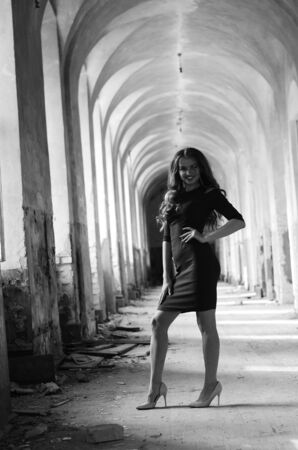 Young beautiful short hair blonde woman in black climbing the stairs, black and white photo. Side view of elegant romantic mysterious lady with movie star look in interior with bricks walls.の写真素材