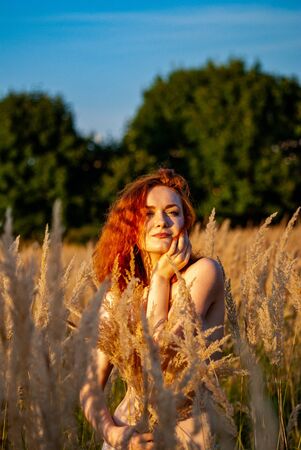 red-haired beautiful girl sits with her back in black, long dress in the grass.の写真素材