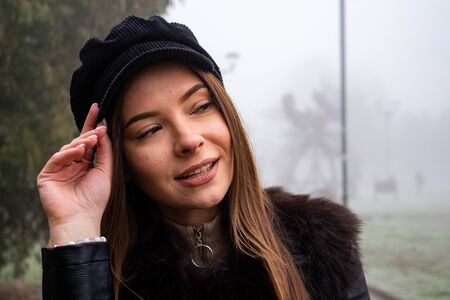 Smiling girl in trench coat walks in park with bouquet of autumn leaves on foggy morning