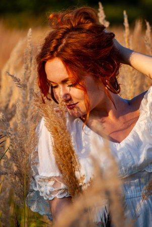 red-haired beautiful girl sits with her back in black, long dress in the grass.の写真素材