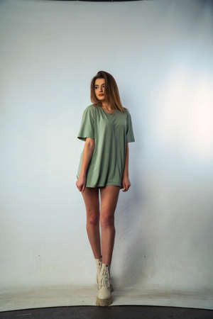 Concept close-up portrait of a pretty girl, young woman with long beautiful brown hair in a green t-shirt on a white background. In the studio in different poses showing emotionsの写真素材