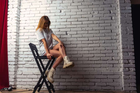 Portrait of a beautiful sensual and sexy blonde girl in a blue dress sitting on a chair against a...