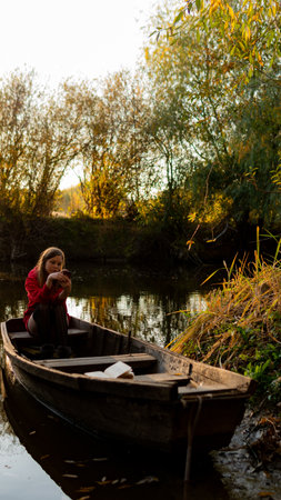 curly girl sitting on the edge of an abandoned wooden boat at sunset.の写真素材