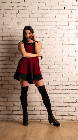 Fashion portrait of woman in red cocktail dress posing for modern magazine. Hand near the face, ring on the finger. Decollete and open shoulder. Dark long hairstyle. Standing in restaurant near vaseの写真素材