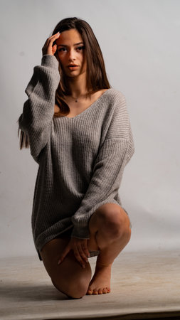 Beautiful young woman sitting on the floor in a gray sweater.の写真素材
