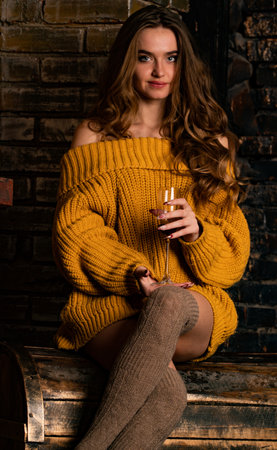 Beautiful girl in a yellow sweater with a glass of wine in her handsの写真素材
