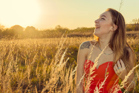 Beautiful young woman in a red dress in a field at sunsetの写真素材
