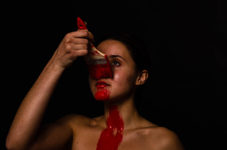 creative portrait of a young girl. The face is painted with red glitter paint. The triangle is drawn on the face. Model in profile on black backgroundの写真素材