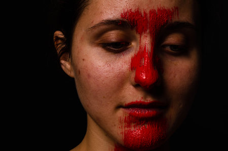 creative portrait of a young girl. The face is painted with red glitter paint. The triangle is drawn on the face. Model in profile on black backgroundの写真素材