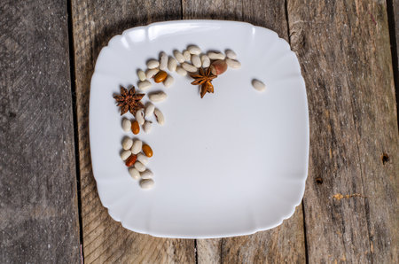 White plate with nuts and spices on a wooden background. Top viewの写真素材