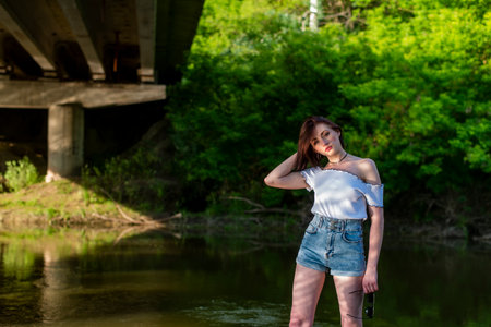 A girl in a white T-shirt and denim shorts is standing on the bank of the river.の写真素材