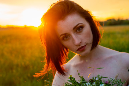 Portrait of a beautiful red-haired girl in the poppies meadow at sunset.の写真素材