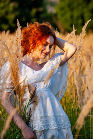 red-haired beautiful girl sits with her back in black, long dress in the grass.の写真素材