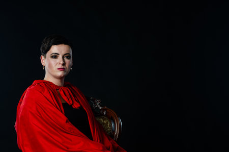 beautiful woman red cloak with red flowers roses in studio. Woman Red Riding Hood. Dramatic and fantastic shooting,fashionable toning. Like a princessの写真素材