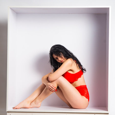 Young woman full body portrait standing near cube. Seductive girl in red lingerie and black boots posing in studio.の写真素材