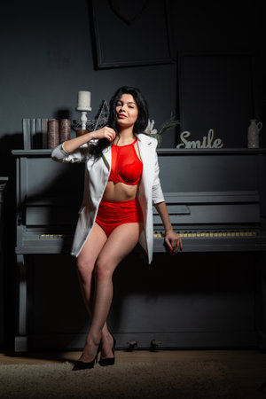 Brunette woman with curly hairstyle standing on a staircase in red underwear.の写真素材