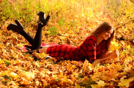 Young beautiful woman relaxing in the autumn park on the ground covered with fallen leavesの写真素材