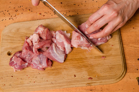 Female hands with a knife in their hand cut fresh meat on a tableの写真素材