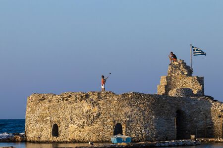 KOS, GREECE - August 30, 2018: Woman takes pictures of her companion with a selfie stick and mobile...