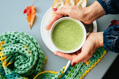 Women's hands and green spinach soup. Top view. Focus on the soup.