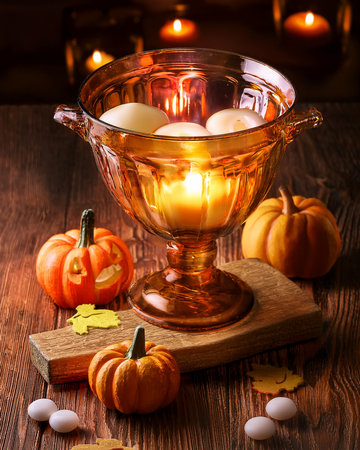 Halloween decoration preparing warm ambiance with burning candles in glass bowl and surrounded by themed pumpkinsの写真素材