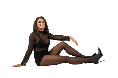 Young woman wearing black sheer top and tights, sitting on the floor, looking at camera and smiling on white backgroundの写真素材