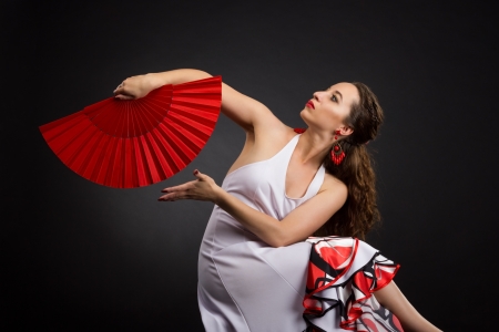 Flamenco dancer in white and red dress with red fan over black backgroundの写真素材