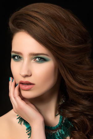 Portrait of beautiful young woman with blue nails and eye makeup touching her faceの写真素材