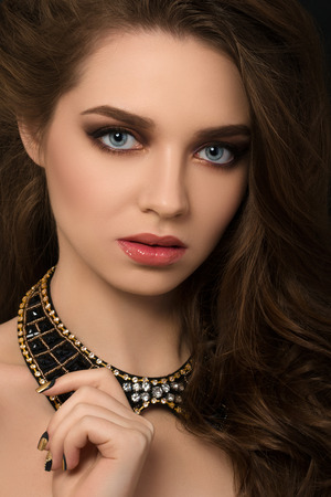 Portrait of young brunette beautiful woman with golden manicure touching her necklaceの写真素材